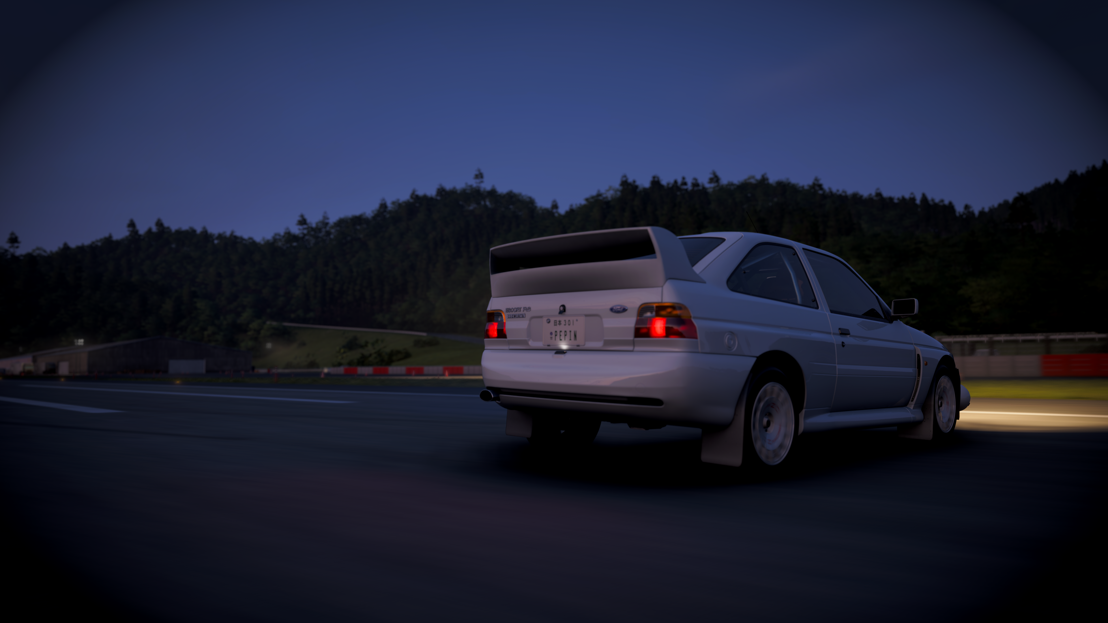 Rear view of 1992 Ford Escort RS Cosworth at night, iconic whale tail showing against a cusp of trees on the horizon