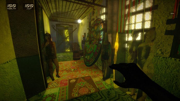 A hallway in G String, the lighting yellowy green. Some kind of large piece of circular stained glass is propped against one wall. There is a patchwork of different coloured, patterned rugs on the floor