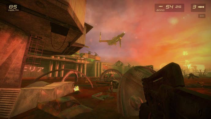 An outdoor shot from G String. There’s a large ship in the sky, which is pink transitioning to orange and yellow. The floor is littered with different bits of circular scrap metal