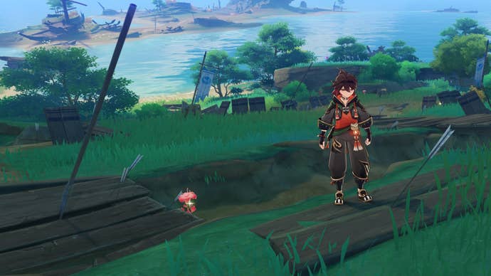 Genshin Impact’s Gaming standing next to a bright red Dendrobium flower, growing in a trench dug into a grassy slope that slants down toward the sea