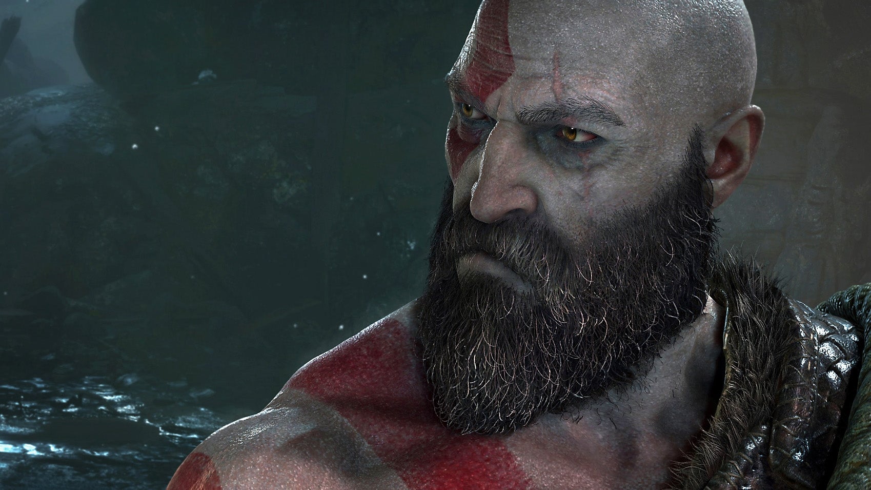 A close-up image of Kratos from the recent God of War games. He is a grey-skinned, beard-toting, bald-guy, with a stern expression and no top on. Mind you, he has the muscles for it. He also has bold red striping across his body and face.