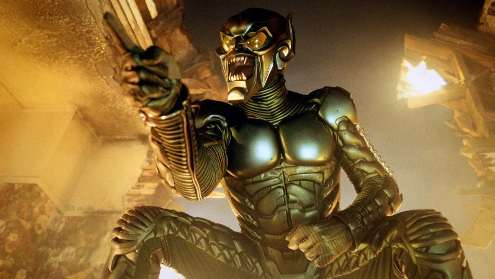 A fully suited Green Goblin villain from Spider-Man - a sort of muscle suit with a grinning enlarged head - points maliciously above the camera, which watches from below.