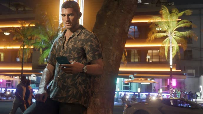 Jason leans against a tree on a neon lit street, using his phone.