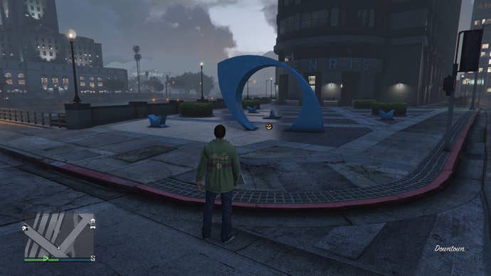 GTA Online, a Jack O'Lantern is sitting below a piece of Blue Modern art near an office building.