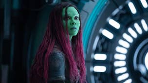 Gamora, a woman with green skin and black hair died pink at the ends, is in a sci-fi room looking at something offscreen in Guardians of the Galaxy 3.