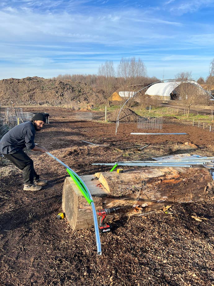 A photograph showing a person hard at work doing something like bending pipes on what looks like farm land. It is, in fact, farm land, and the person is Hades Lestary.