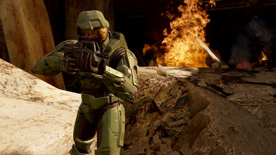 Master Chief aims a gun as he traverses a rocky landscape.