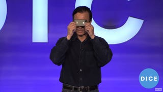 On-stage at DICE, Trip Hawkins holds an iPhone up very close to his face, covering both eyes.
