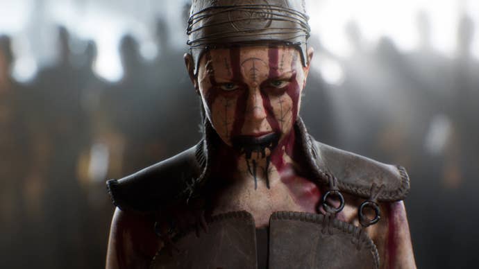 Hellblade 2’s Senua stood looking into the camera, her face adorned with red paint in thick lines going across it.