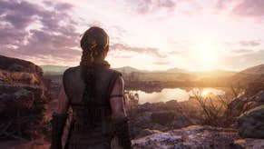 A screenshot from behind the character Senua, who's looking out at the horizon as the sun sets behind hills and a lake. The sky is turning pink.