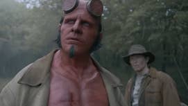 Hellboy is stood in the woods looking concerned into the distance, a man with a similar expression behind him in Hellboy: The Crooked Man.
