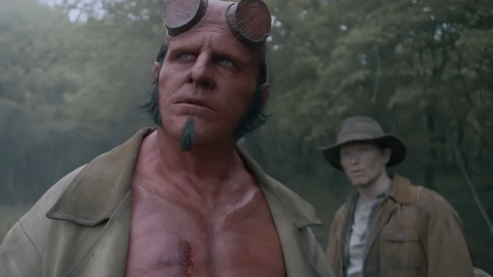 Hellboy is stood in the woods looking concerned into the distance, a man with a similar expression behind him in Hellboy: The Crooked Man. - 1