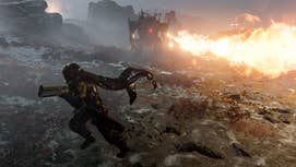 Helldivers 2 screenshot showing a player character in a futuristic military suit with a cape, holding a gun, running away from a large robot firing a flamethrower on a rocky planet.