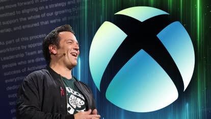 Xbox CEO Phil Spencer standing next to a giant, circular Xbox logo. It looks a bit as though he's singing it into existence.