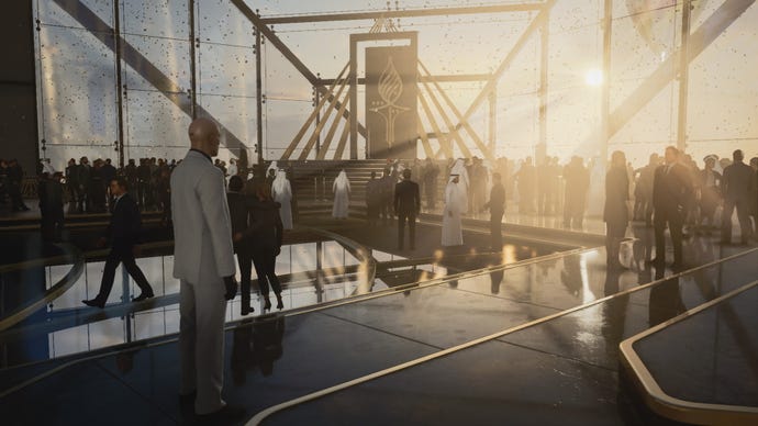 A screenshot of Agent 47 standing in a large glass atrium from Hitman 3’s Dubai level