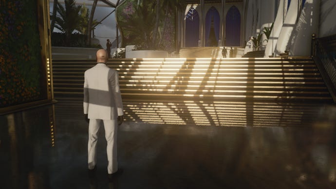 A screenshot of Agent 47 standing in front of a shiny set of stairs in Hitman 3’s Dubai level