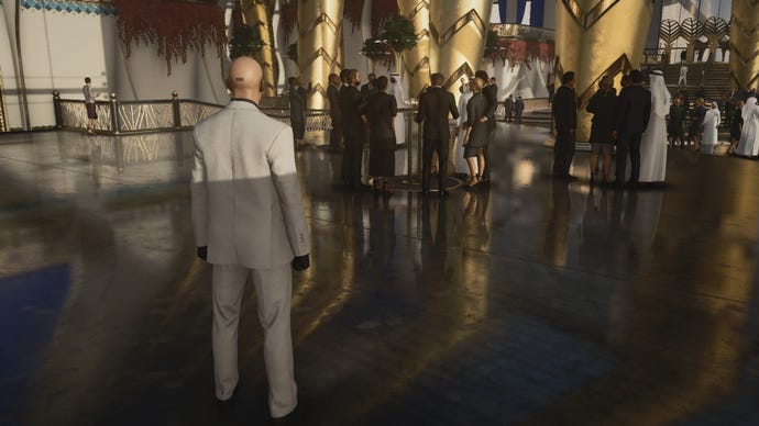 A screenshot of Agent 47 standing in a shiny reception hall from Hitman 3’s Dubai level