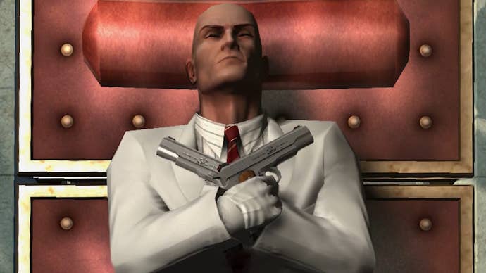 Agent 47 lies, presumably ‘dead’. He is wearing a white suit with a red tie. He has two guns in his hands, which are laid across his chest