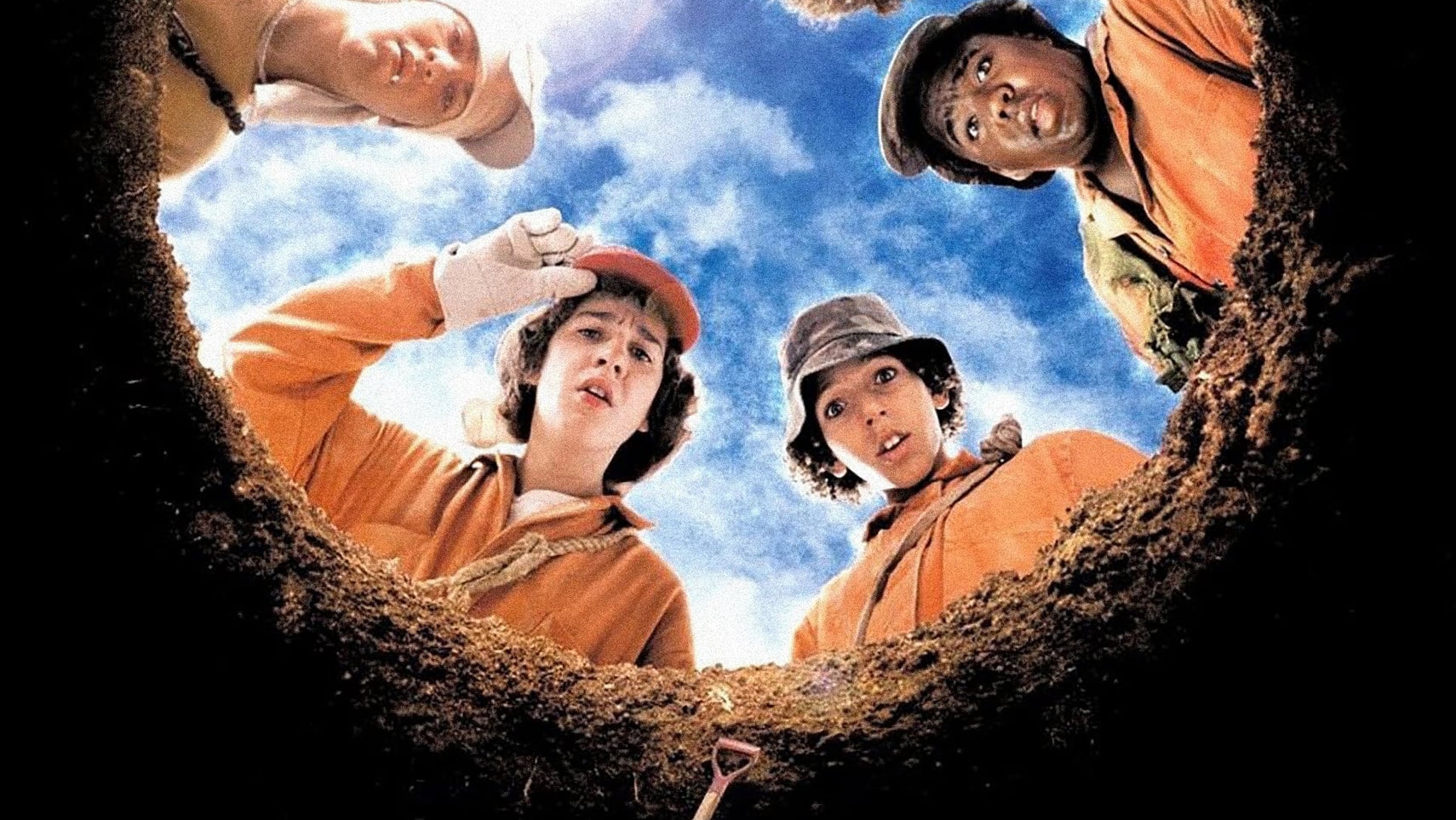 Shia LaBeouf and other characters looking down a hole, the camera looking up at them, in a poster for Holes. They are all wearing orange jumpsuits. - 1