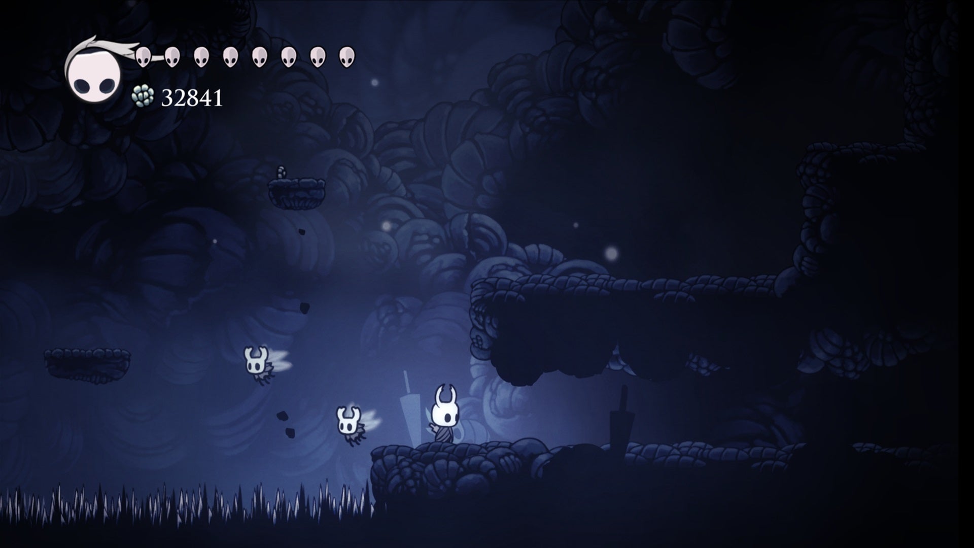 The titular knight protagonist stands by a nail, marking the entrance to a hidden chamber in Hollow Knight. - 4