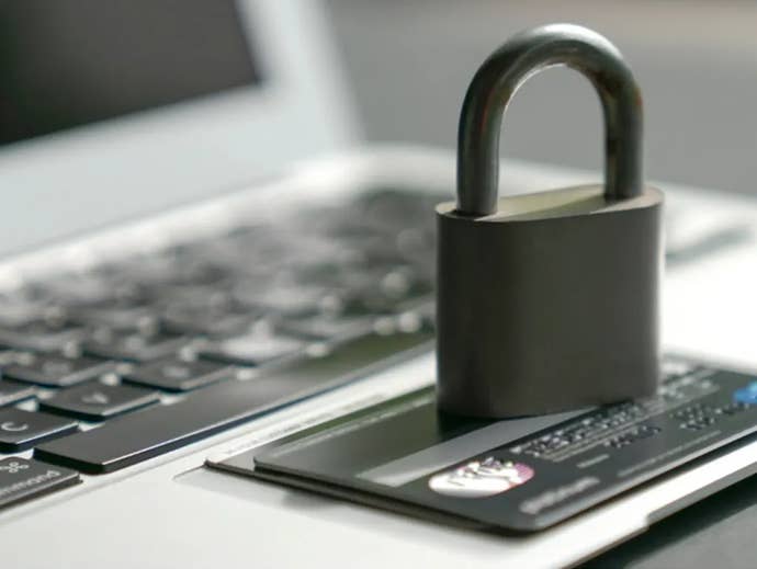 A lock sits on top of a credit card, on top of a laptop.