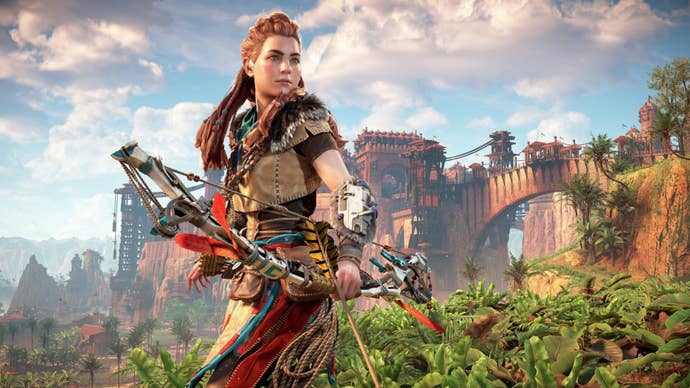 Aloy in Horizon Zero Dawn Remastered, she’s stood holding her bow and arrow, a bridge and town seen in the background.