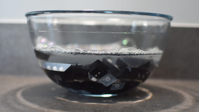 A bowl of removed keyboard keycaps, soaking in soapy water.