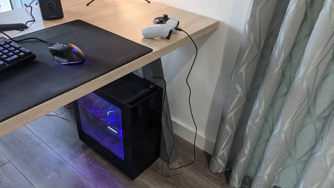 A PS5 controller connected to a gaming PC via a USB cable.