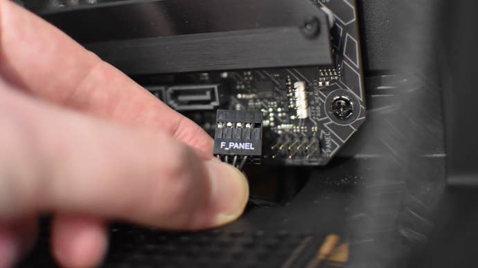A front panel connector cable is held in front of its corresponding motherboard header.