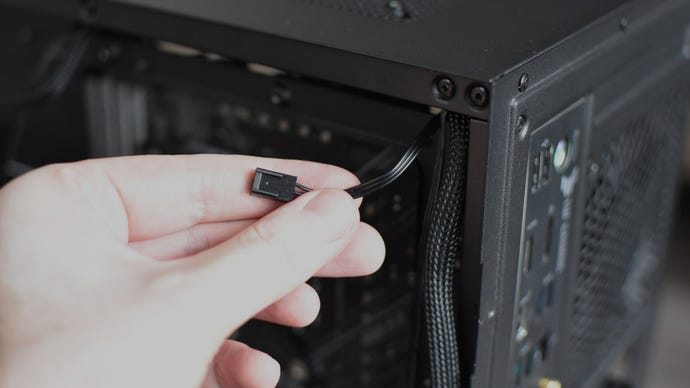 The motherboard connection cable of a case fan, being pulled through a cable routing hole.