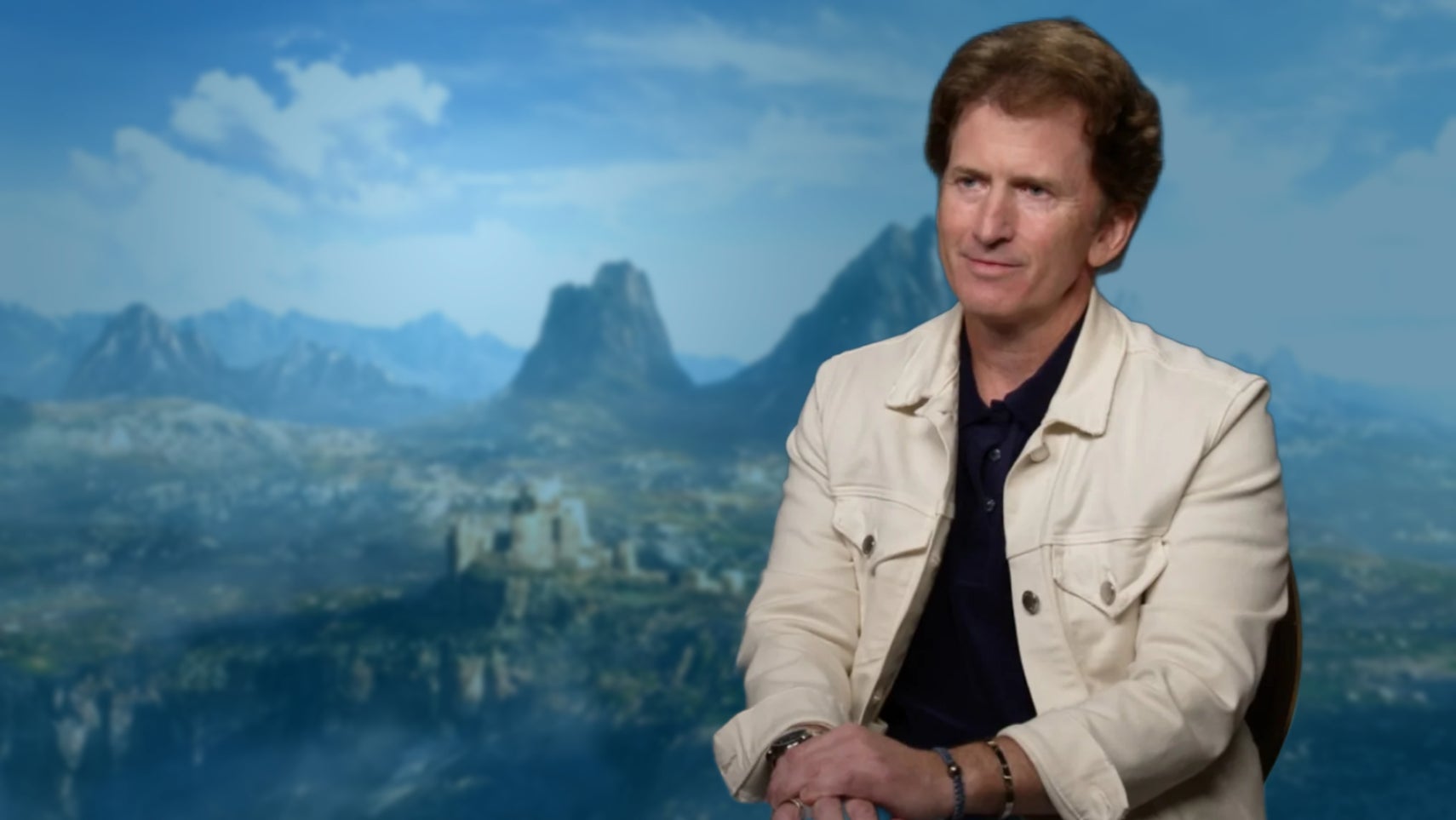 Todd Howard, in a cream jacket, over the top of a mountainous and verdant valley as shown in a teaser for The Elder Scrolls 6