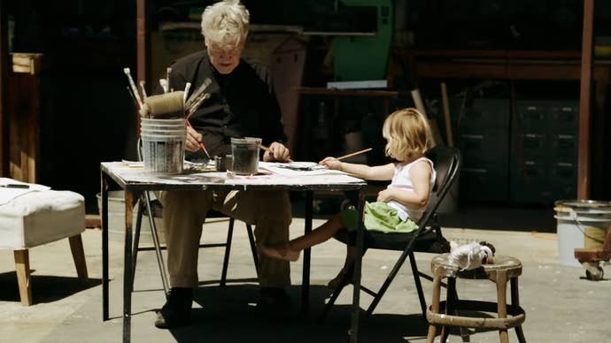 David Lynch and a child sit at a table filled with art supplies working on some art in this screen from the documentary, David Lynch: The Art Life.