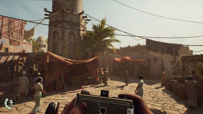 The player holds a camera as they observe an Egyptian village.
