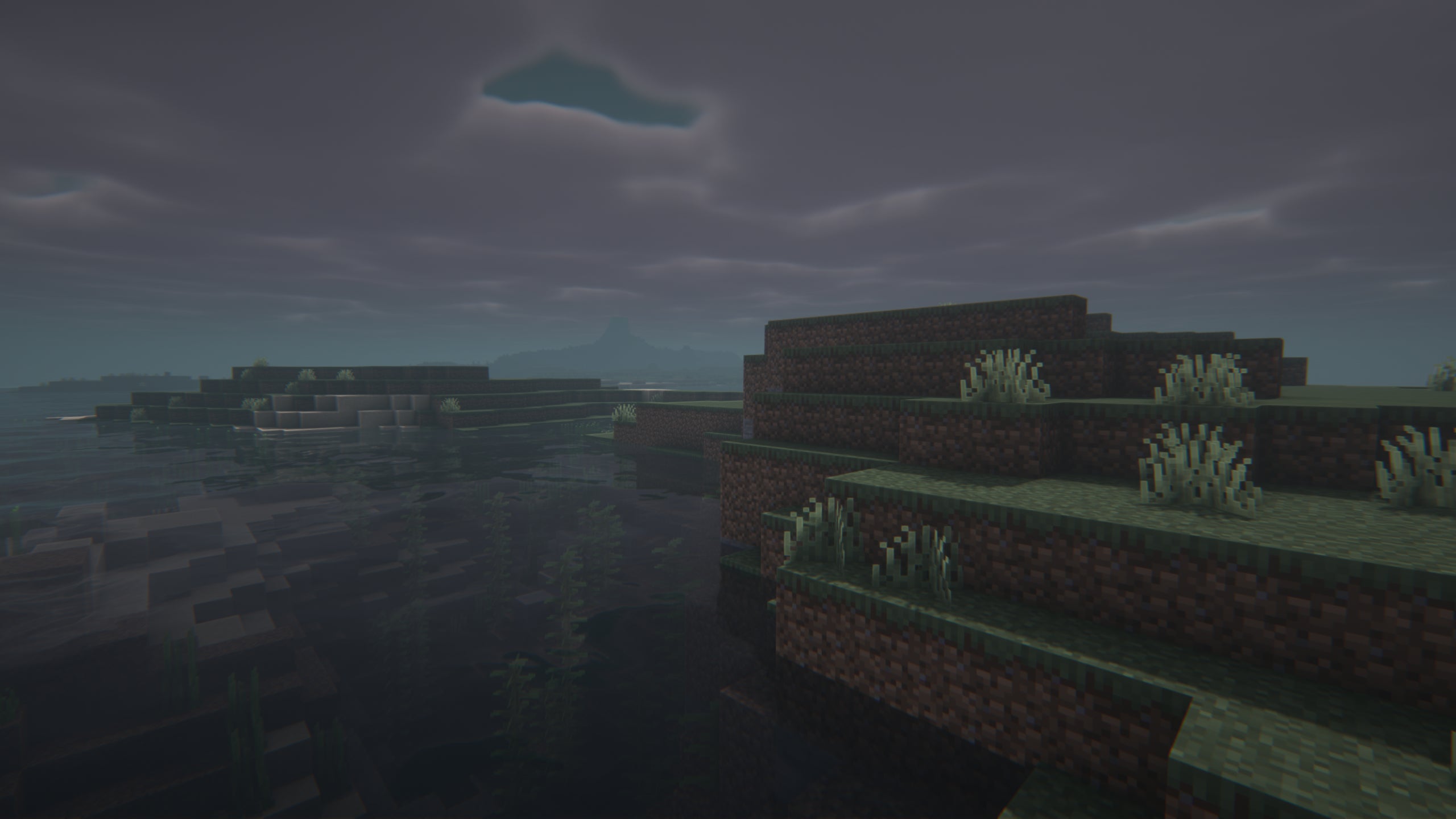 Close-up of some grass next to a river in a foggy Minecraft landscape showcasing Insanity Shaders.