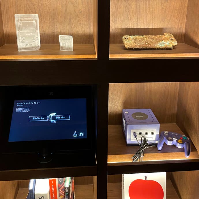 A bookshelf with what looks like a gold-encrusted Nintendo Switch, and another with a GameCube in.