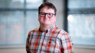 Jamie Brittain, leader writer on Maverick Games' upcoming unrevealed open world game - a white man with short brown hair, black-rimmed glasses and wearing a salmon and blue tartan shirt