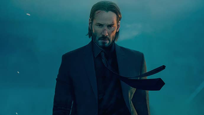 Keanue Reeves as John Wick, he’s a bit beaten up, it’s smokey around him, his tie being blown by the wind.