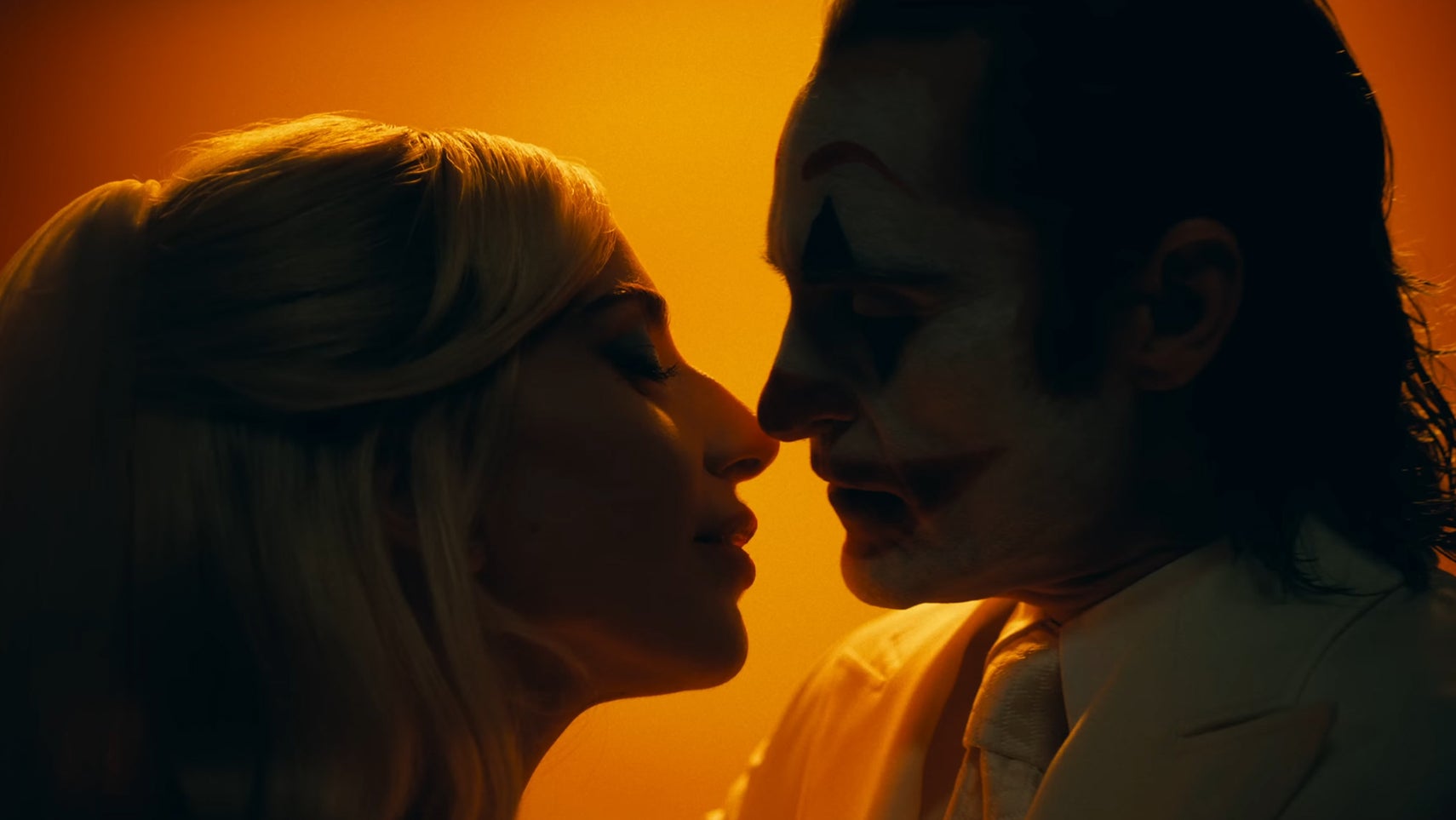 A still from Joker 2 showing Lady Gaga and Joaquin Phoenix as Harley Quinn and The Joker about to kiss, silhouetted by an orange light. - 1