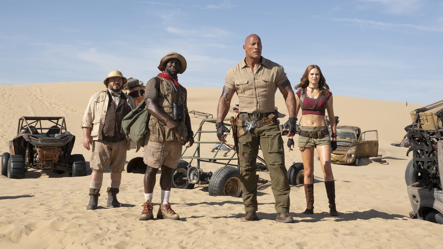 The cast of Jumanji all stood in a desert, various cars surrounding them. - 1