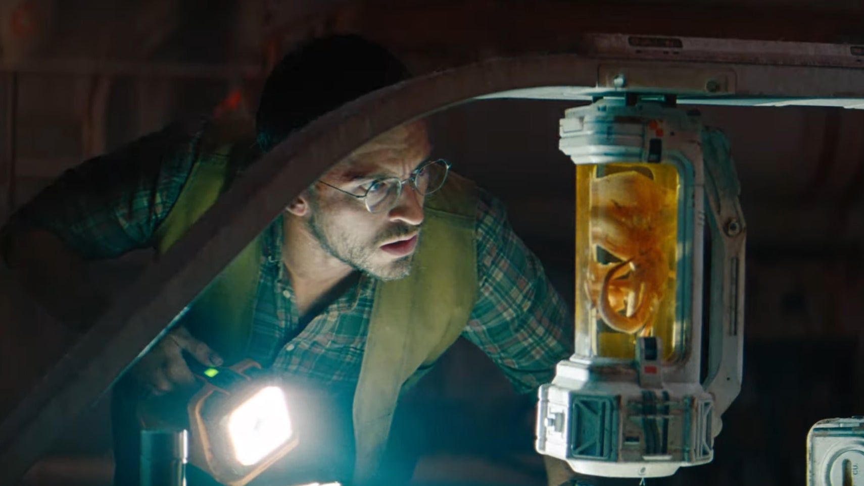 Jonathon Bailey in Jurassic World Rebirth looking at some kind of small pod with a dinosaur-like creature preseverd in a yellow liquid. - 1