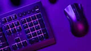 A PC keyboard and mouse are illuminated in purple light on a desk