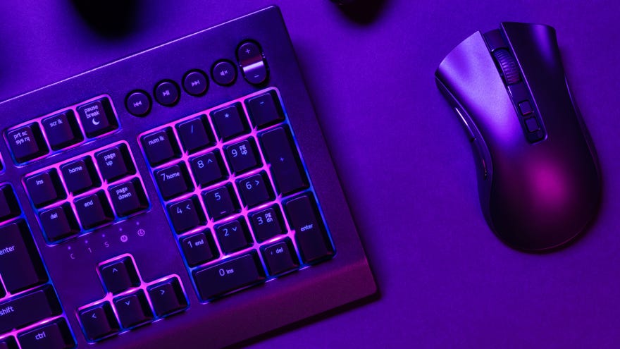 A PC keyboard and mouse are illuminated in purple light on a desk