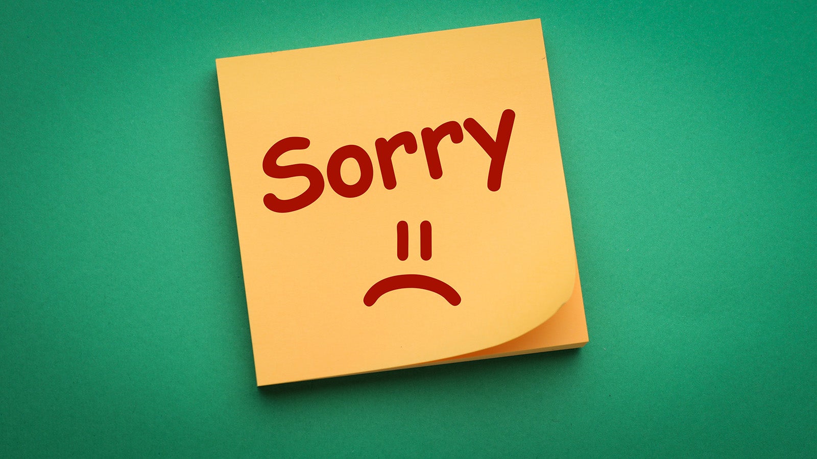 The word "Sorry" written in big red lettering on a square yellow post-it note, with an upside down smiley face - a frowney face - below it. Someone's in trouble.