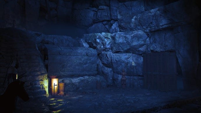 El interior de un kofun en Assassin's Creed Shadows. Está oscuro, con una pequeña luz de la linterna la única iluminación. Se puede ver un gran cofre entre la penumbra.