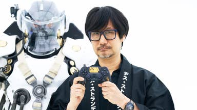 Hideo Kojima holding a Death Stranding 2 themed PS5 controller in front of a statue