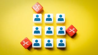 An image showing nine cubes with simple people silhouettes on, while around them, red cubes with scissor images on close in. It's an image that's meant to represent layoffs.