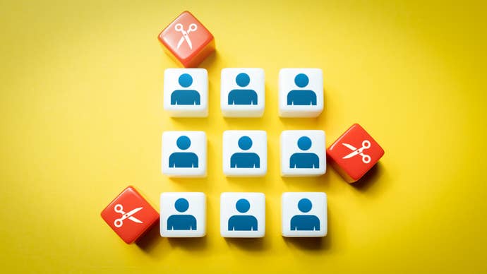An image showing nine cubes with simple people silhouettes on, while around them, red cubes with scissor images on close in. It’s an image that’s meant to represent layoffs.
