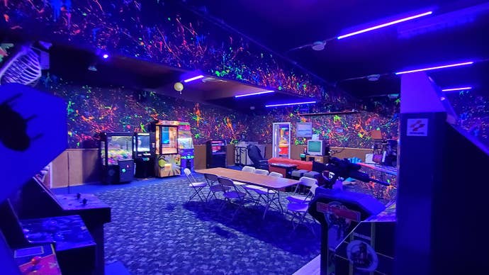 The inside of Legends Arcade. A darkened room with neon paint splattered on the walls that’s lined with arcade cabinets.