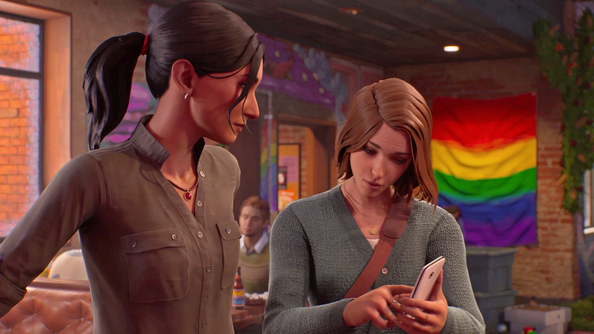 Max and Safi examine Max's phone, with a large pride flag swag hanging from the wall behind them. - 8