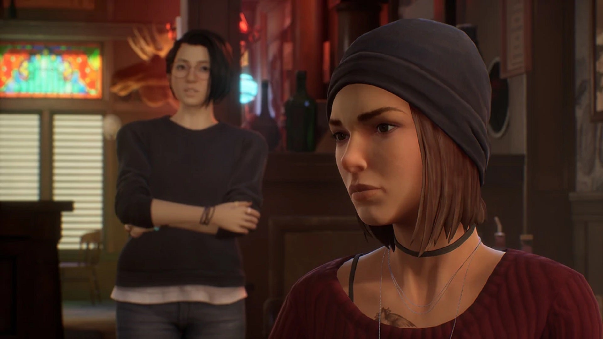 A screenshot from Life Is Strange: True Colors shows a scene from the Black Lantern tavern, with Steph sitting in the foreground and Alex standing a way behind her. - 3